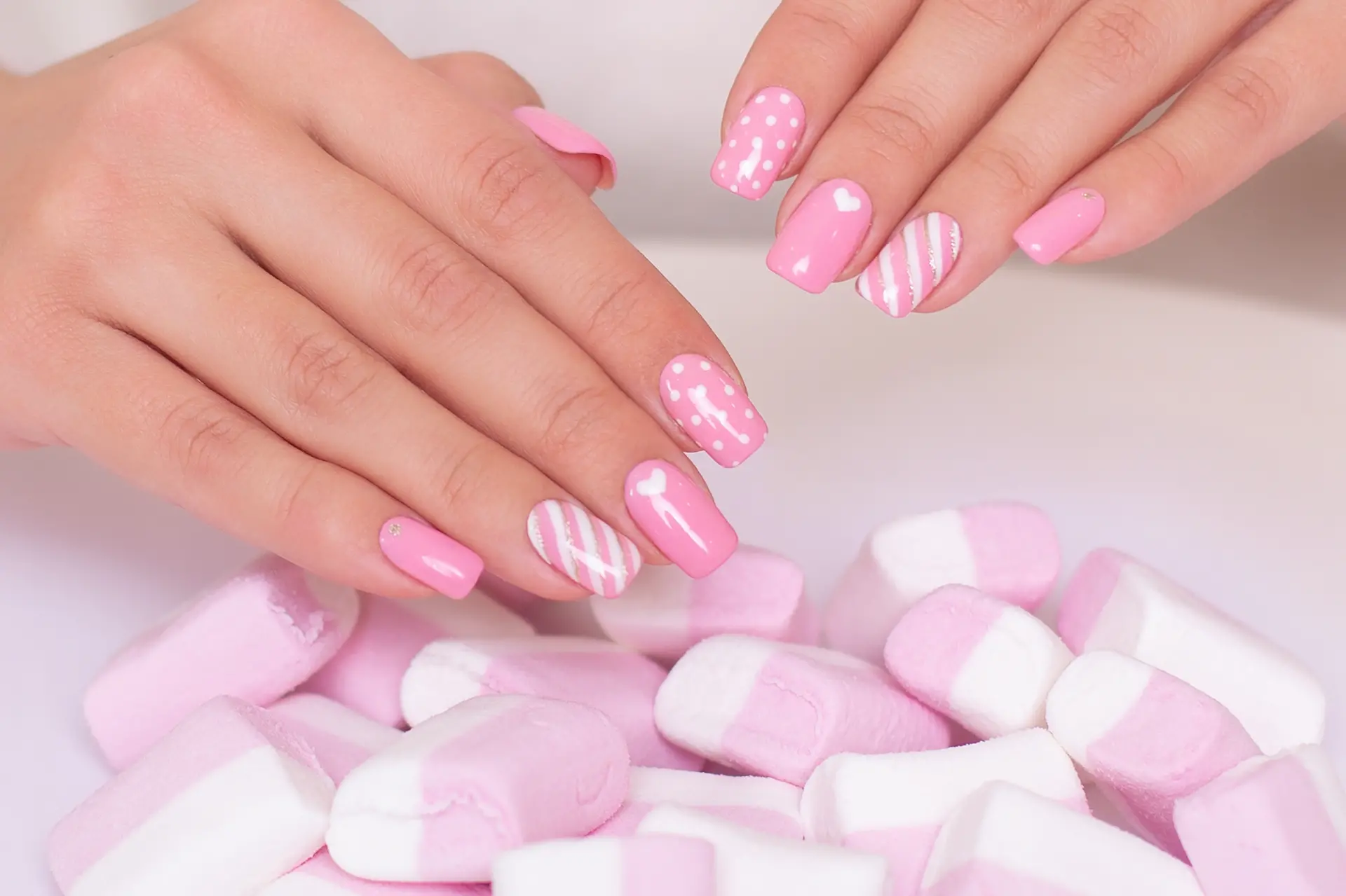 female-hands-with-pink-manicure-nails-hearts-design-marshmallow-background